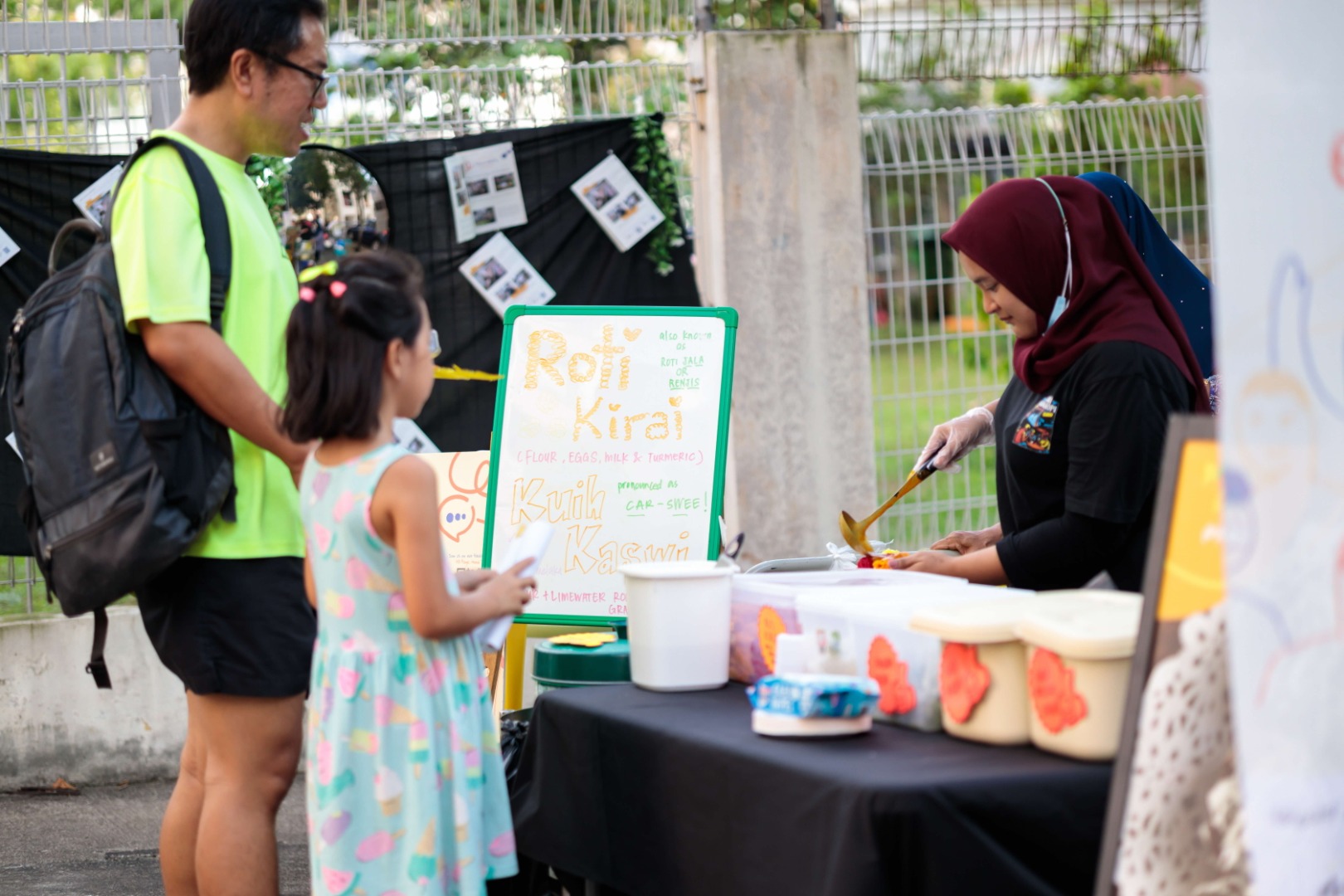 A street food woman serving a traditional Malay food to a parent and his child.